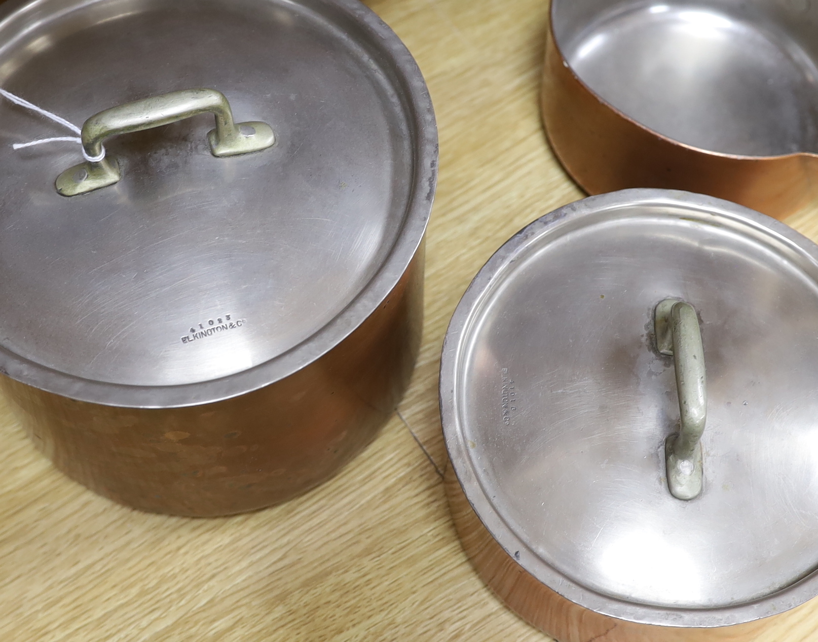 Three copper saucepans and two frying pans by Elkington and Co including two graduated pans with lids, the largest 46cm wide